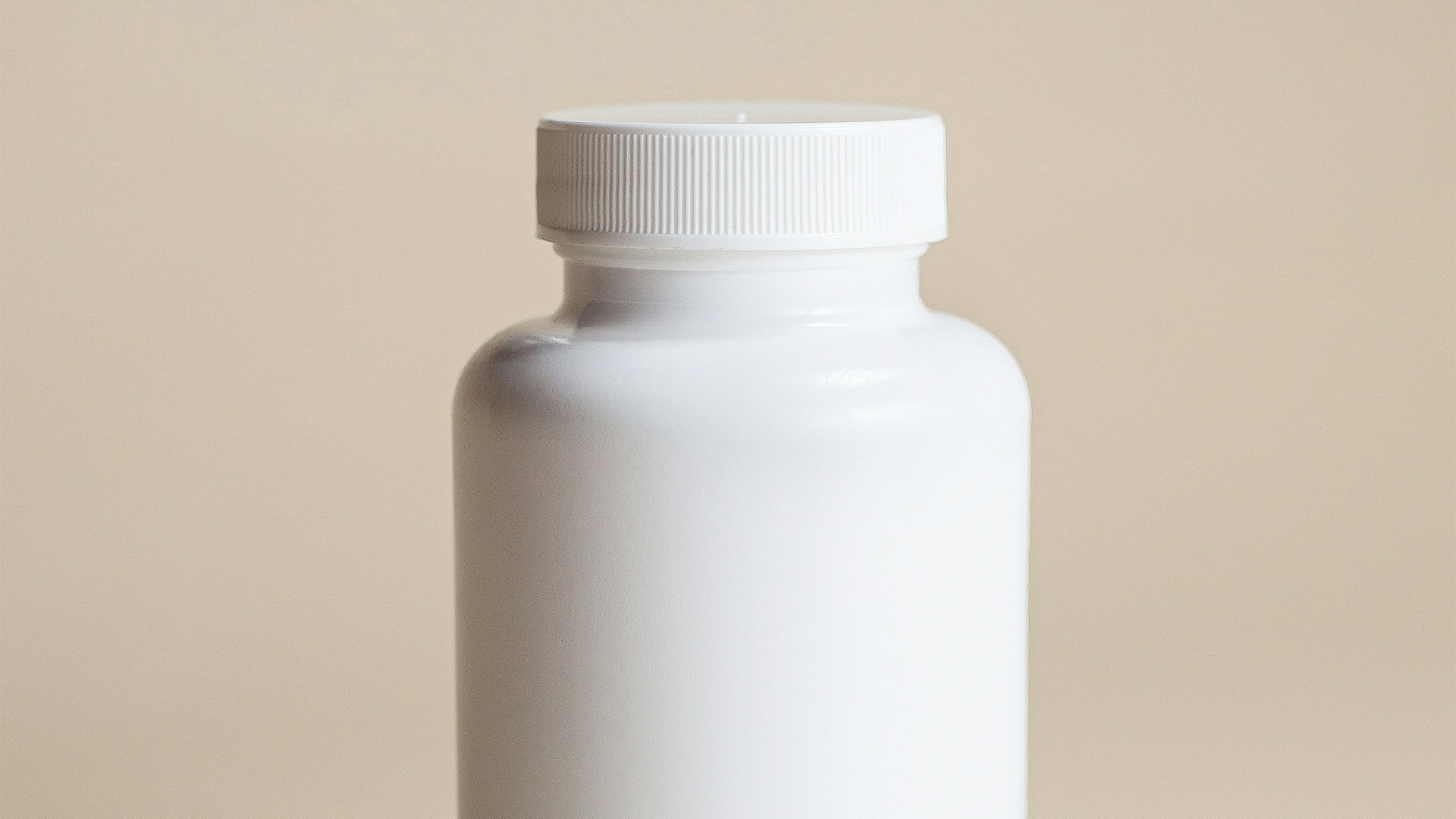 The cap and shoulder of a plain white plastic supplement bottle with a ridged cap, against a beige background.