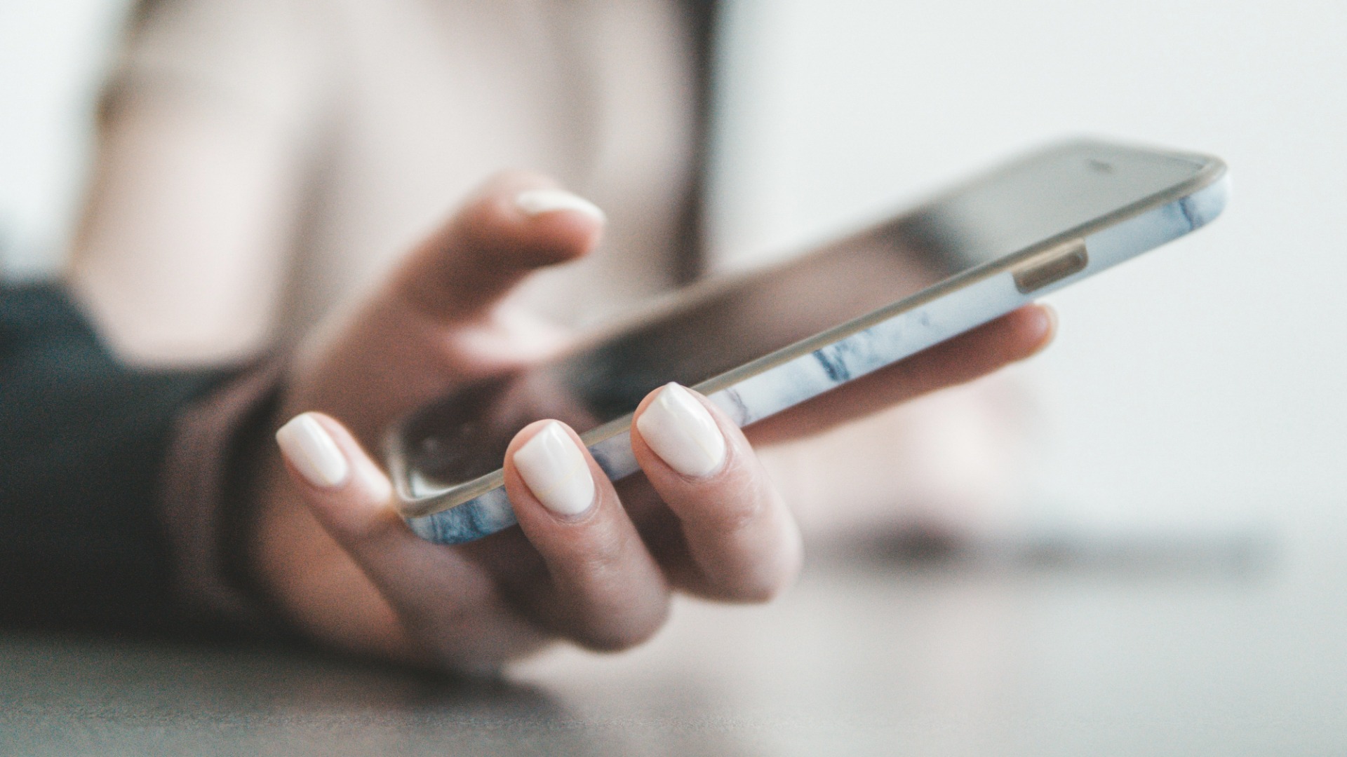 A hand holding a smartphone with a marble-patterned case, the screen turned away and the background out of focus.
