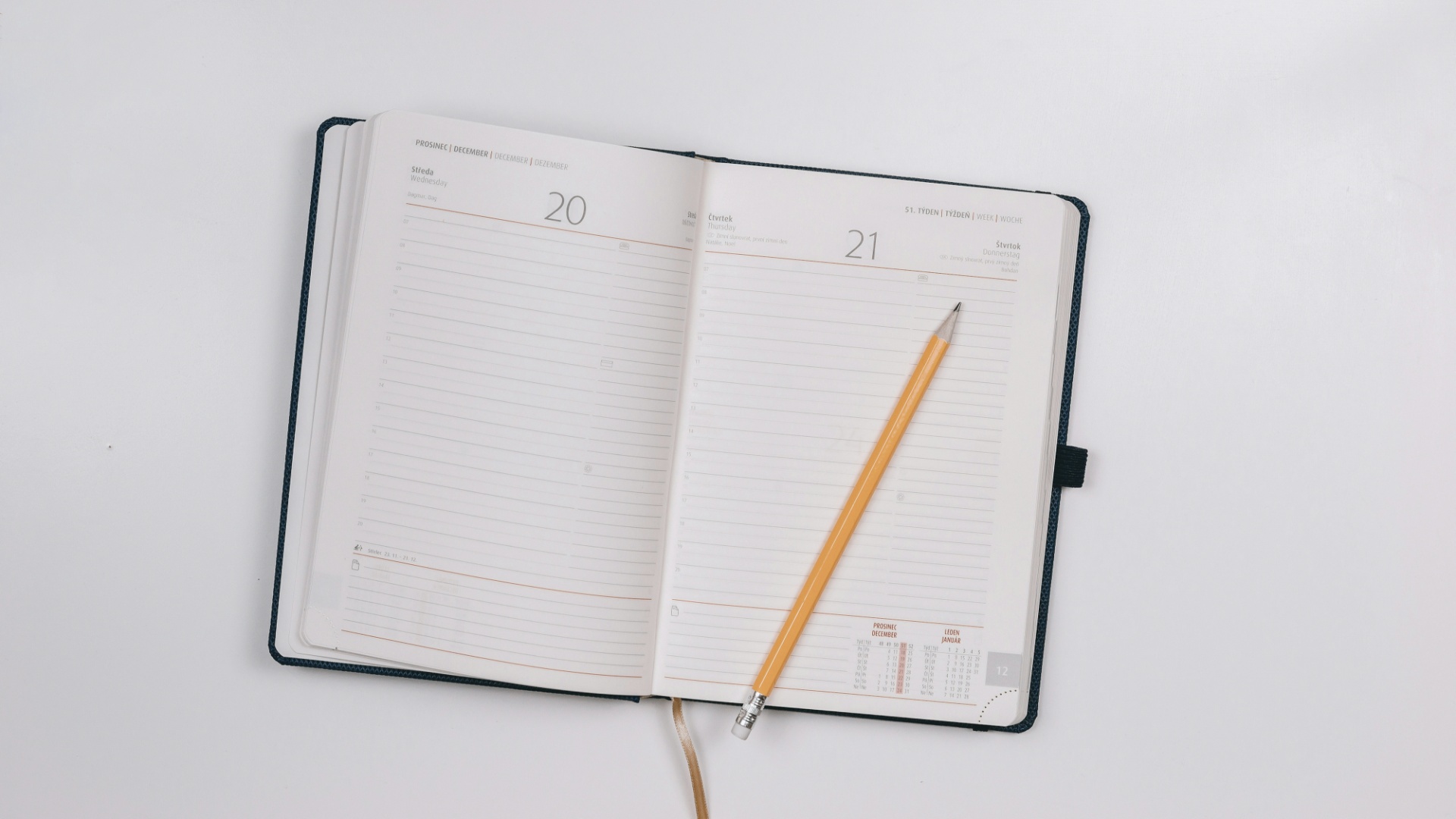 An open day planner with a yellow pencil lying across the right-hand page, on a plain white surface.
